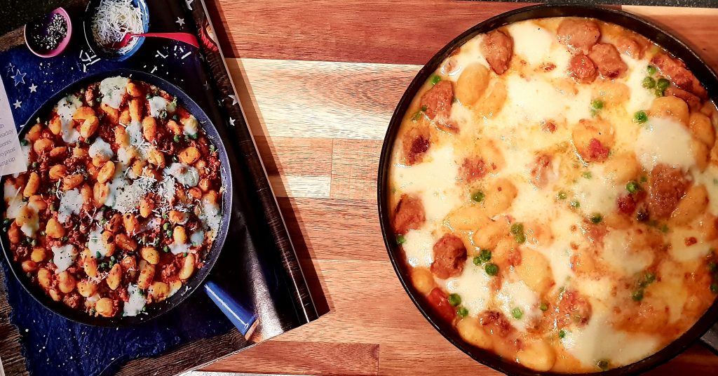 Pan of sausage gnocchi bake next to a magazine on a board