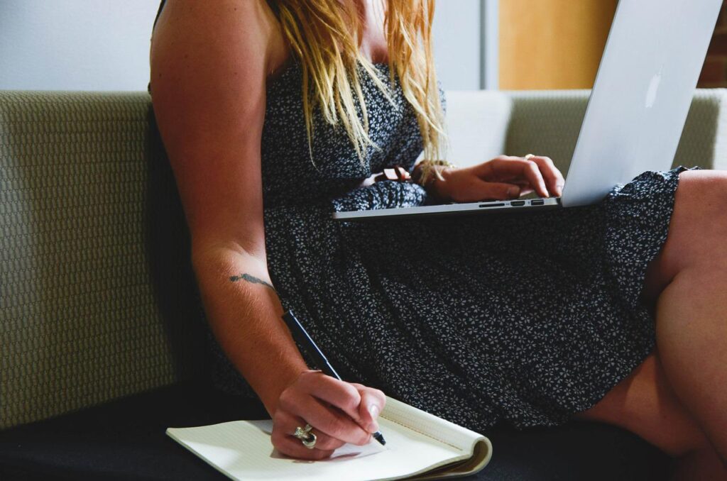 Woman on laptop also writing down notes