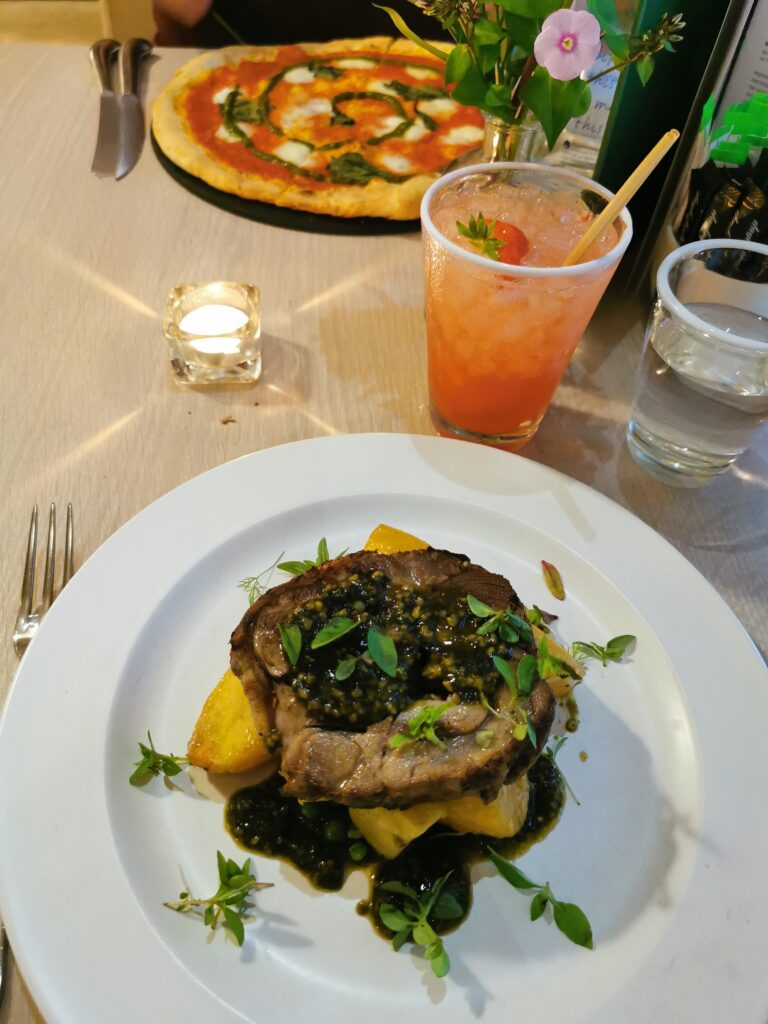 Shoulder of lamb on roasted new potatoes with a herby pesto with a heritage tomato wood fired pizza in the background