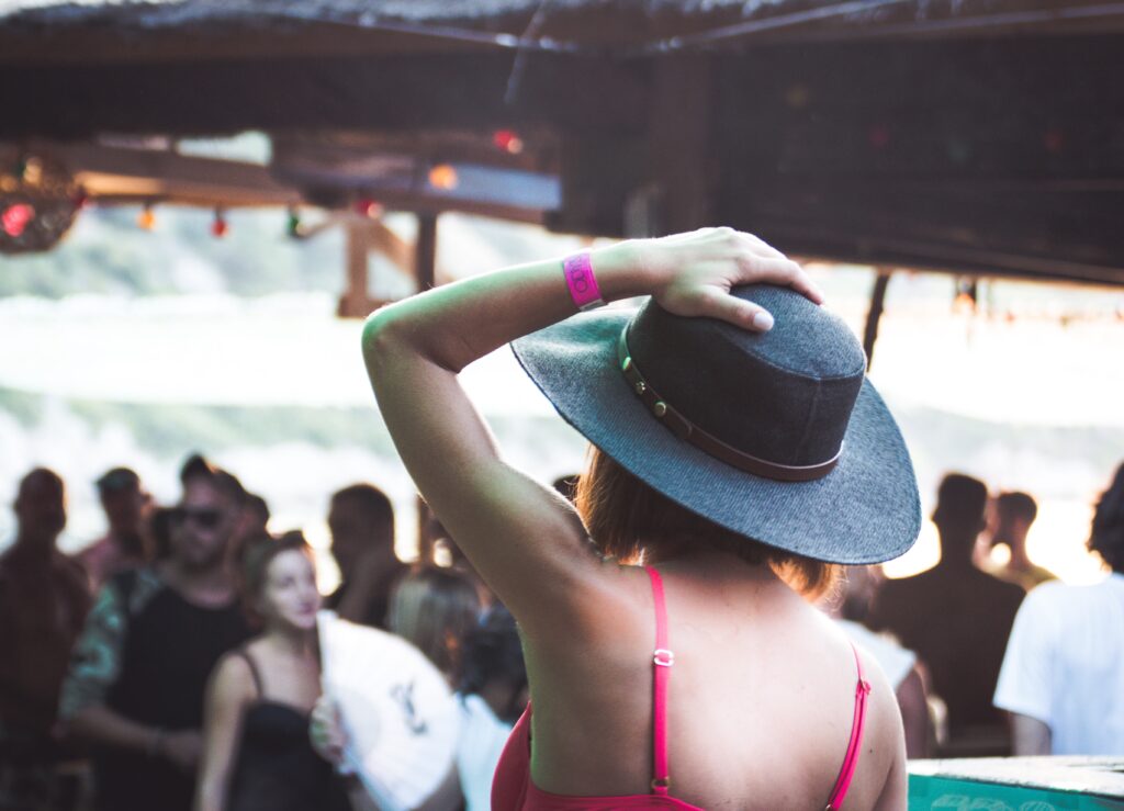 Woman at festival holding on to a grey fedora hat on her head