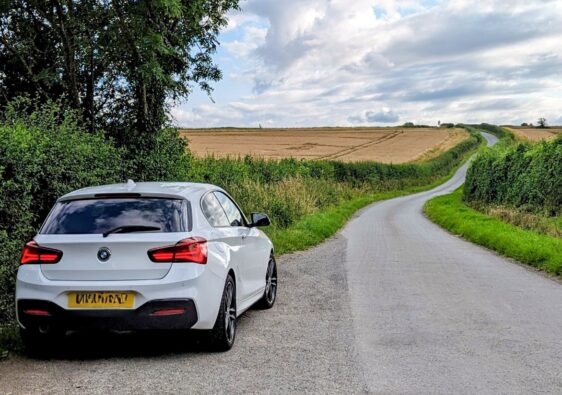 A white BMW 1 series parked in a layby on a country road